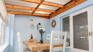 Zona pranzo con tavolo in legno, sedie bianche, un vaso con fiori e una parete con un salvagente e un quadro incorniciato.