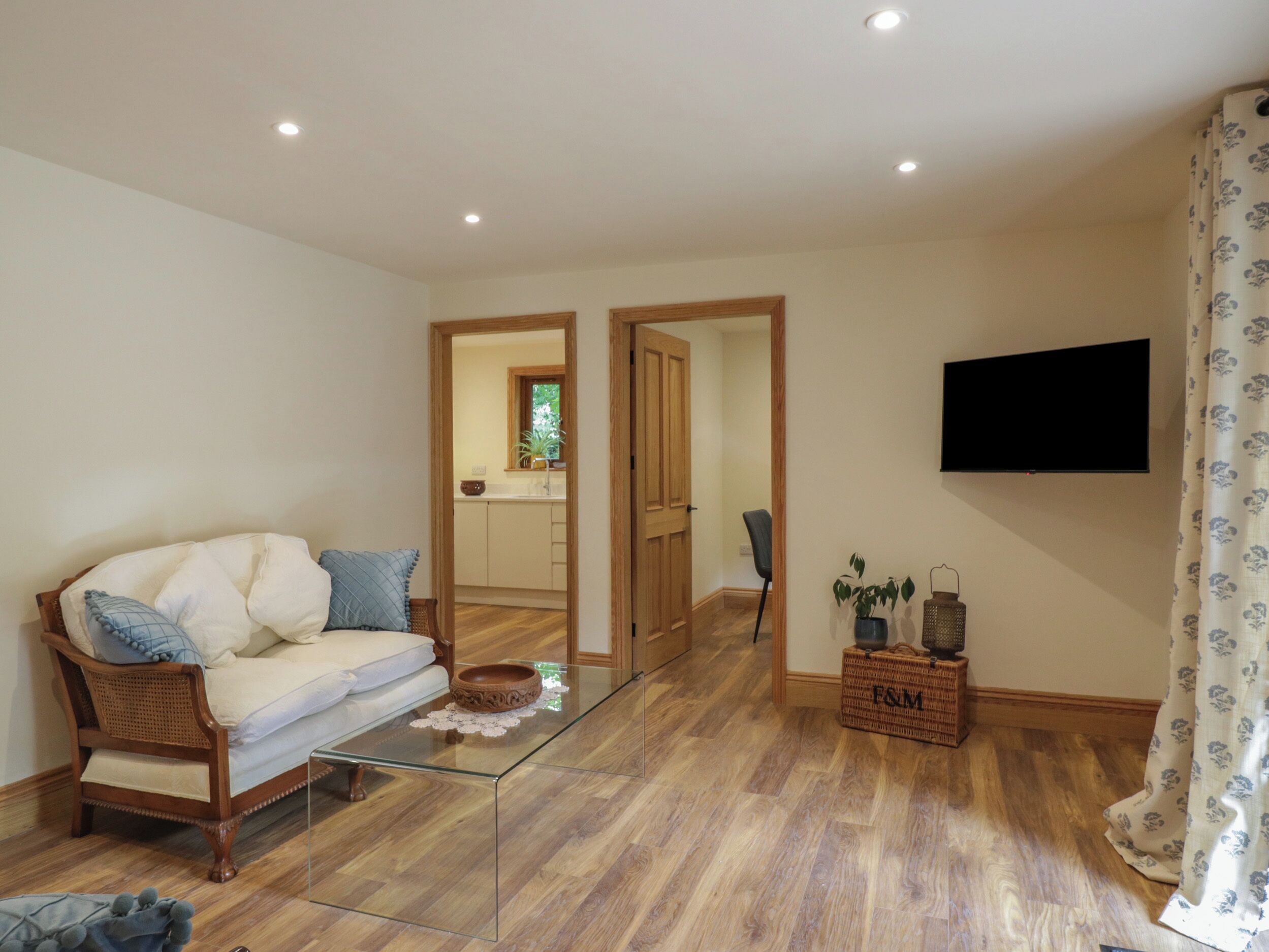 Ein Wohnzimmer mit einer Couch, einem Glastisch, einem an der Wand befestigten Fernseher und Holzboden.