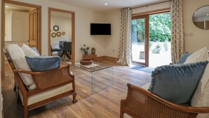 Un salon meublé avec des meubles en osier, une table basse en verre et une grande porte-fenêtre coulissante donnant sur un espace extérieur.