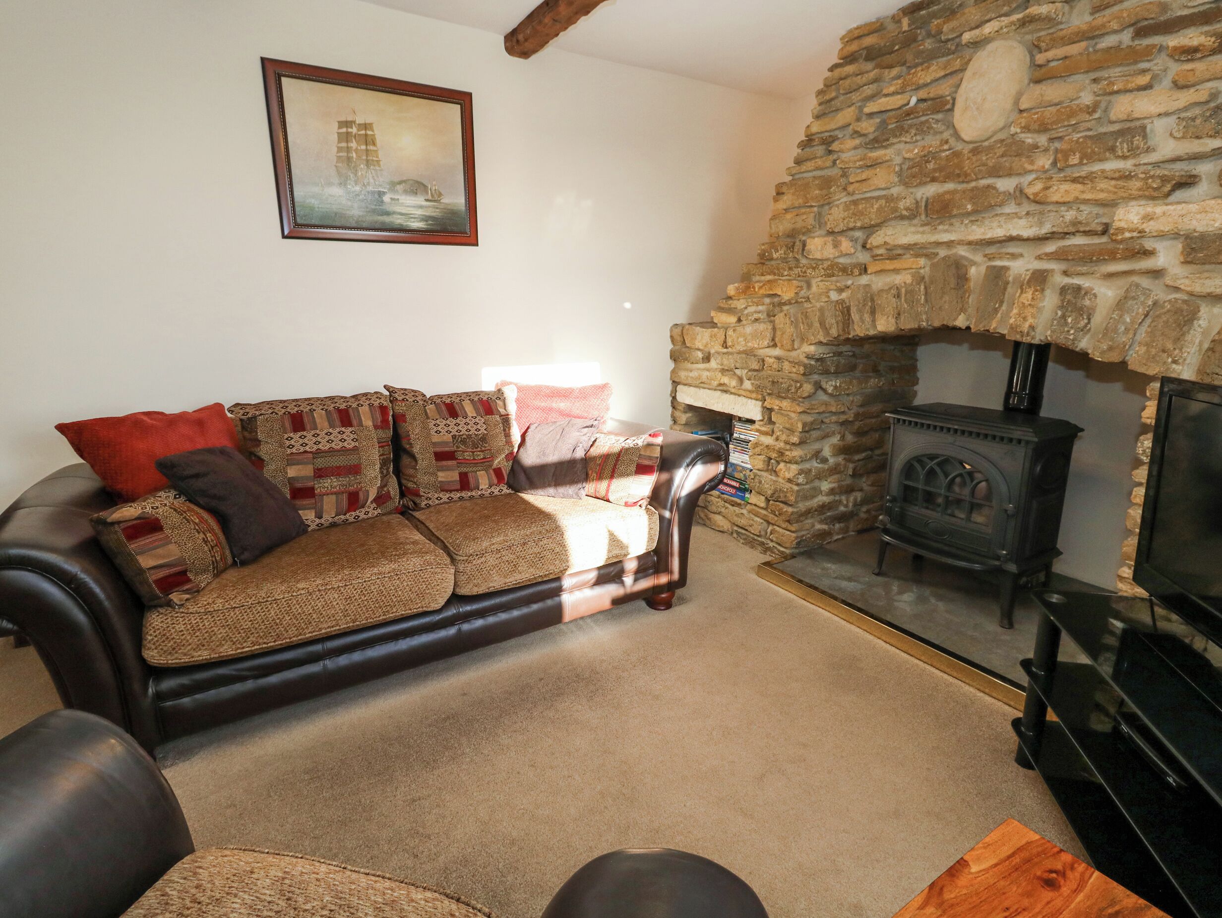 A cozy living room with a stone fireplace, a leather sofa, and a framed picture on the wall.