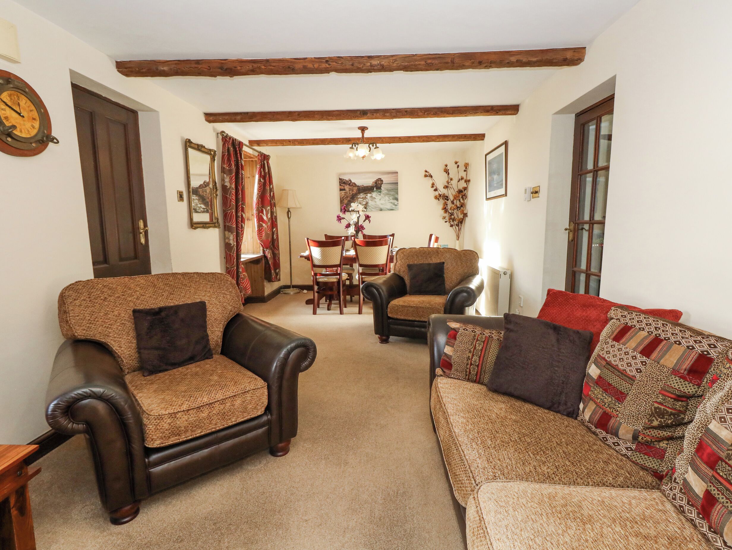 A cozy living room with a brown leather sofa, a patterned armchair, and a red and patterned couch. A dining area with a table and chairs is visible in the background.