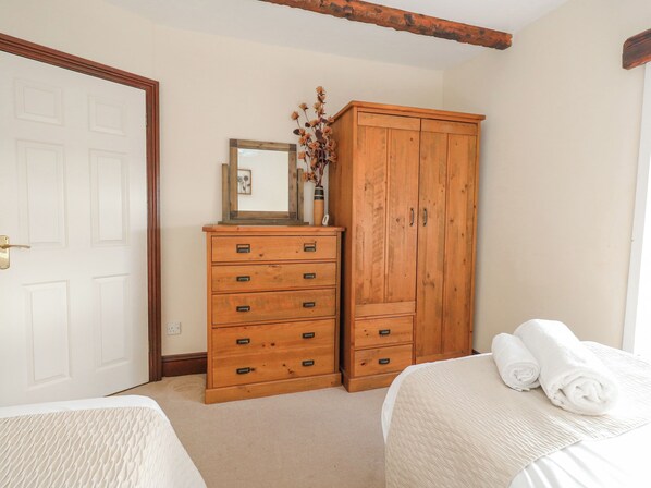 A bedroom with two beds, a wooden wardrobe, a mirror, and a vase with dried flowers.