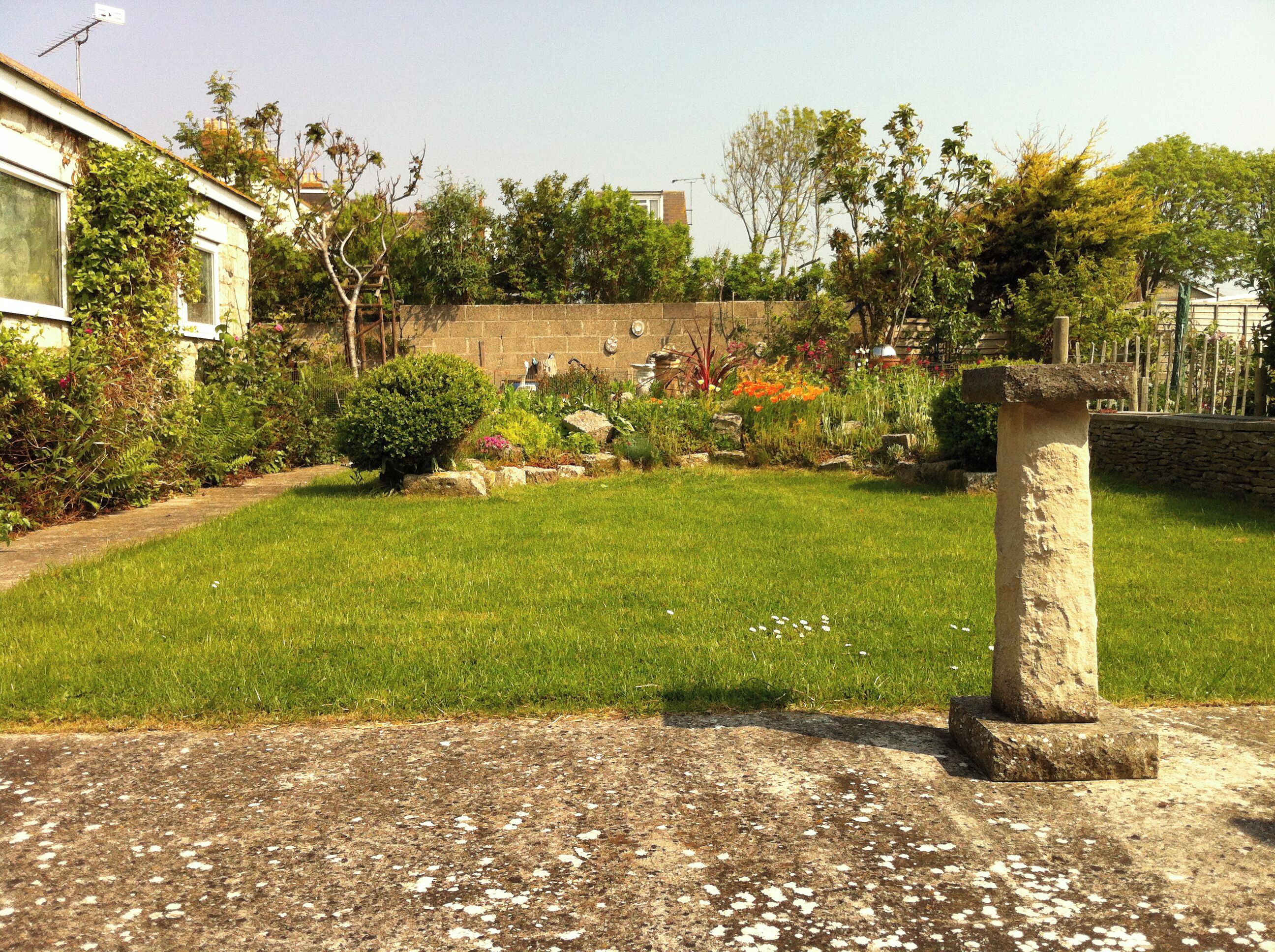 A garden with a stone pillar, a grassy lawn, and a brick wall.