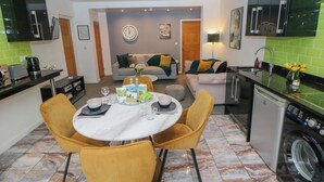 A modern kitchen with a dining area, a washing machine, and a living room with a sofa and a clock on the wall. - Number 4 Westmoreland (Matlock)