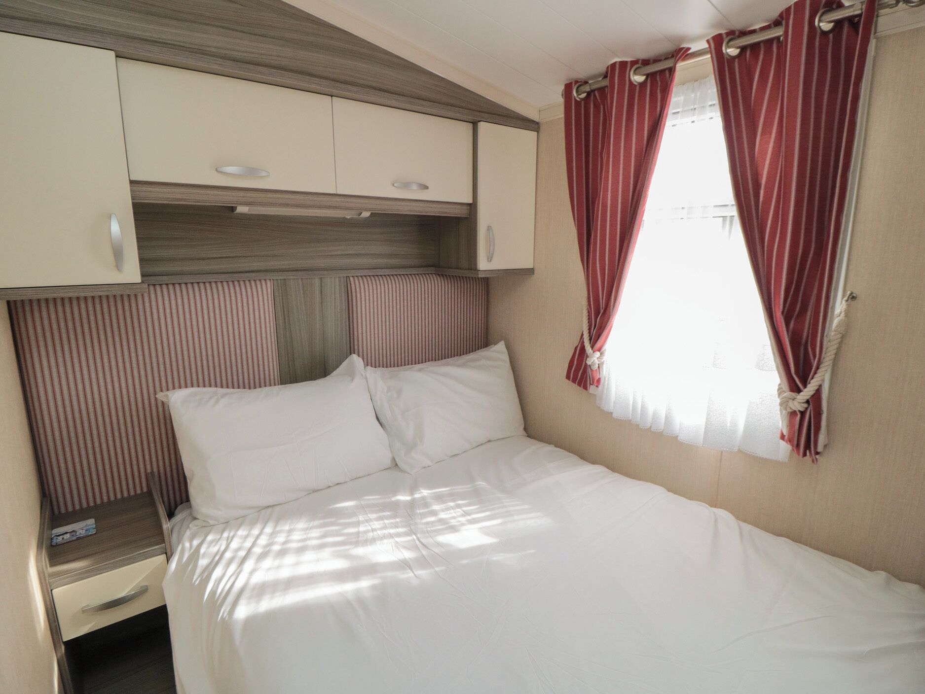 A bedroom with a bed, a nightstand, a wardrobe, and a window with curtains.