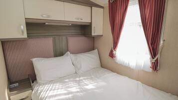 A bedroom with a bed, a nightstand, a wardrobe, and a window with curtains.