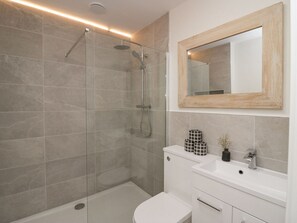 A modern bathroom with a glass-enclosed shower, a white toilet, and a vanity with a mirror and sink. - Driftwood Cottage (Ulverston)