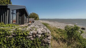 A modern building with large windows, a stone pathway leading to the beach, and a view of the sea. - Driftwood Cottage (Ulverston)