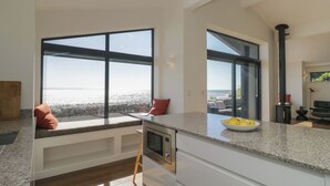 A modern kitchen with large windows, a built-in stove, and a view of the sea. - Driftwood Cottage (Ulverston)