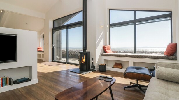 A modern living room with a fireplace, large windows, and a cozy seating area. - Driftwood Cottage (Ulverston)