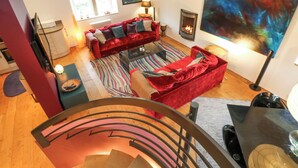 A spacious living area with a red sofa, a fireplace, and a large abstract painting. - Byre Suite (Skipton)