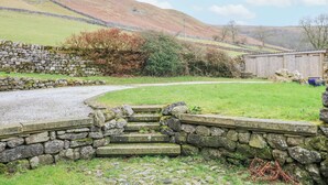 A rural landscape with stone walls, a gravel path, and a wooden structure in the background. - Byre Suite (Skipton)