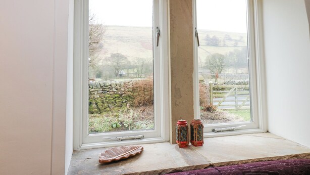A room with two windows overlooking a rural landscape, a stone wall, and two decorative lanterns on the windowsill. - Byre Suite (Skipton)