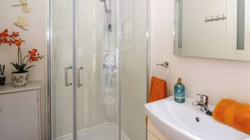 A bathroom with a glass-enclosed shower, a white sink with an orange towel, and a mirror above the sink.
