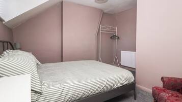 Ein Schlafzimmer mit einem Bett, einem Nachttisch, einem roten Sessel, einer Heizung und einer Deckenleuchte.