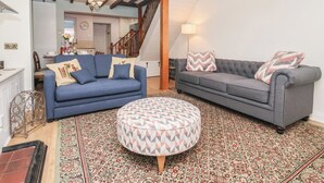 A living room with a blue sofa, a grey sofa, and a patterned ottoman. There is a staircase leading to another room.