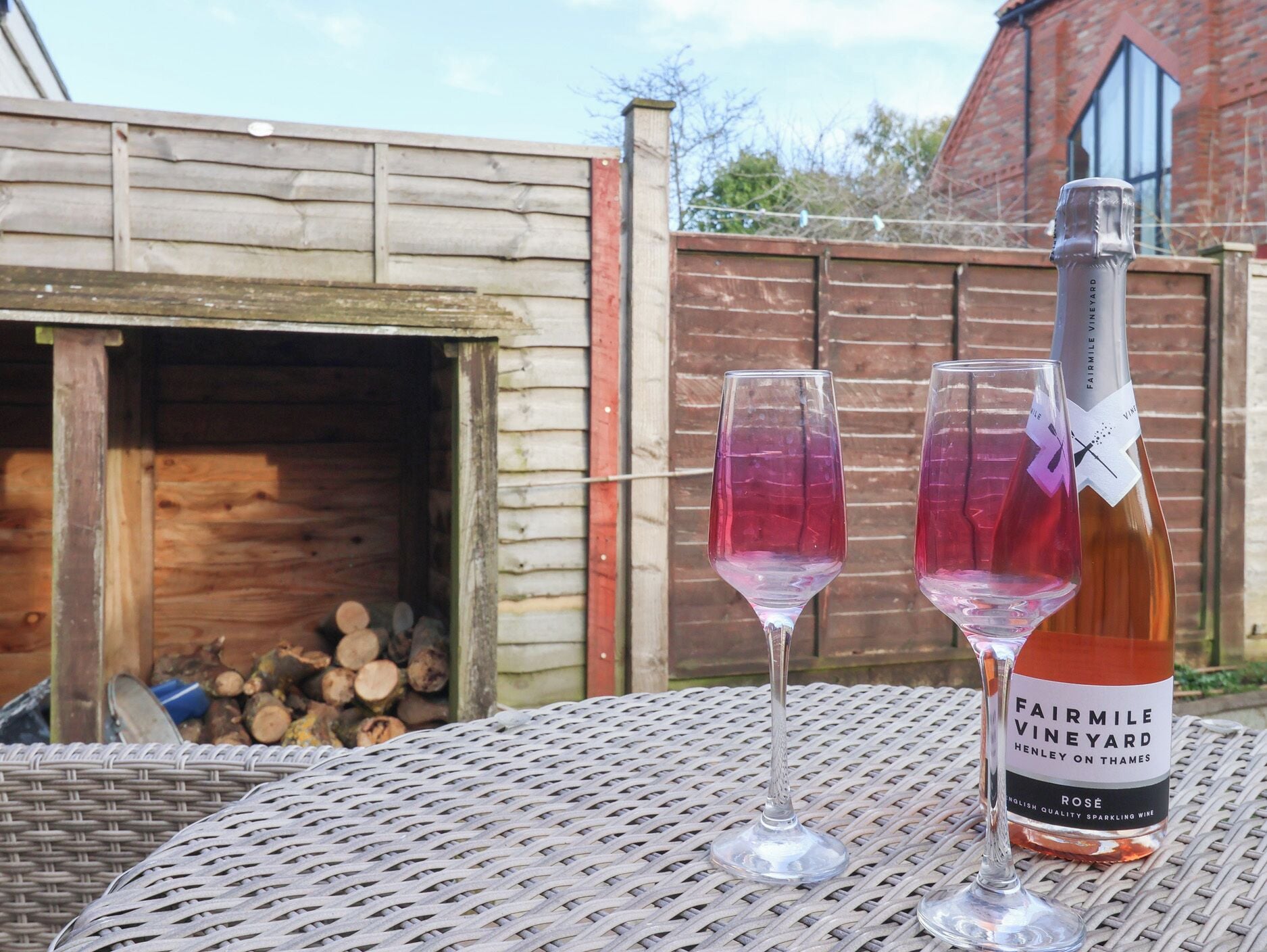 Een fles Fairmile Vineyard Rosé wijn en twee glazen op een rieten tafel buiten.