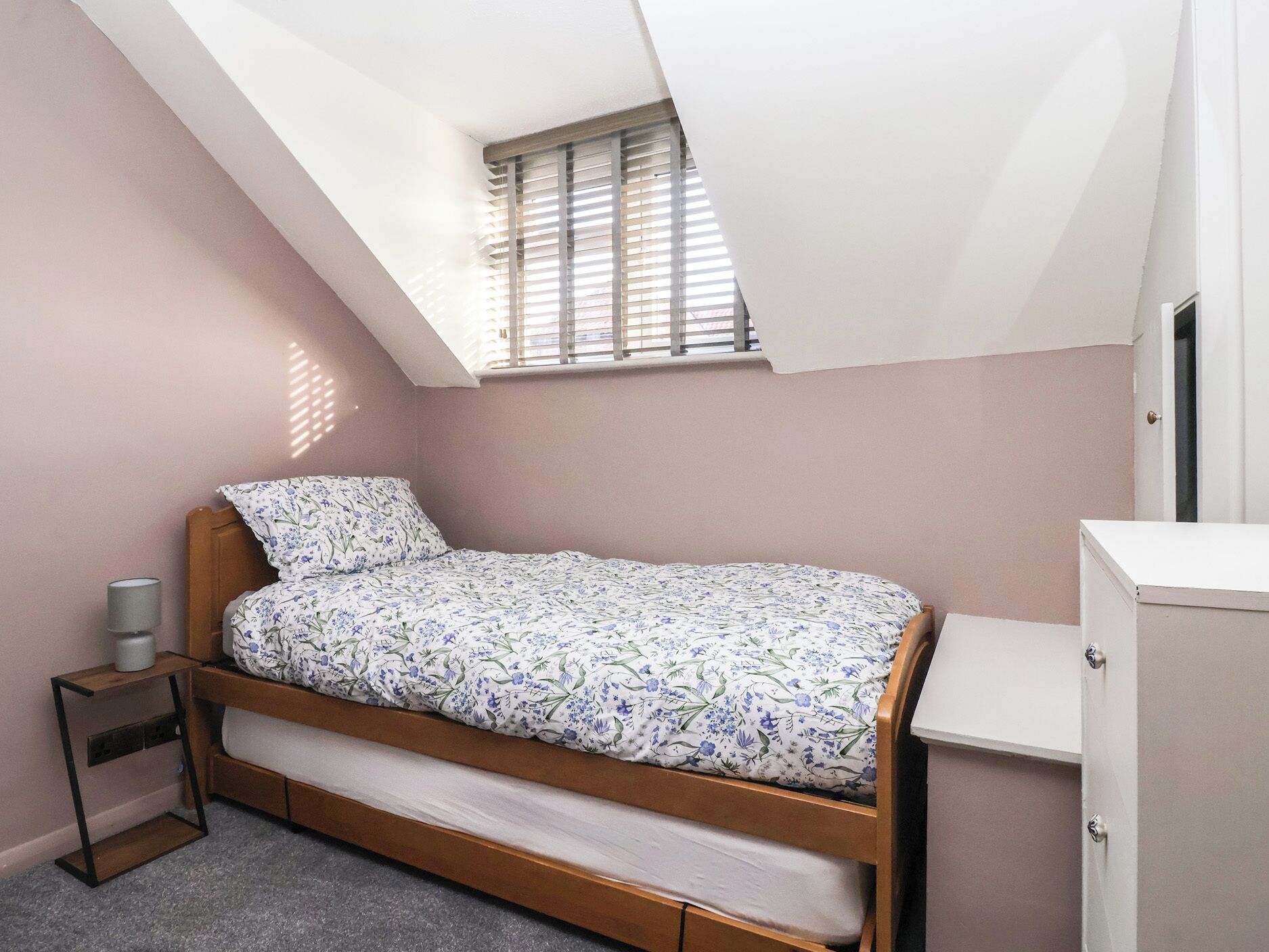 Ein kleines Zimmer mit einem Einzelbett, geneigter Decke und Dachfenster, einem Nachttisch und einem Kleiderschrank.