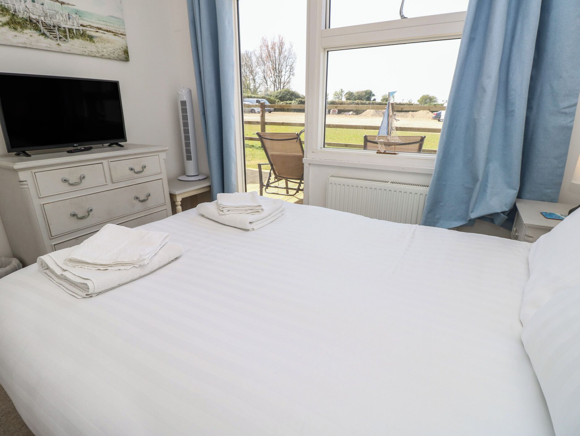 A hotel room with a bed, a TV, a desk, a chair, and a window with a view of a lawn and a building.