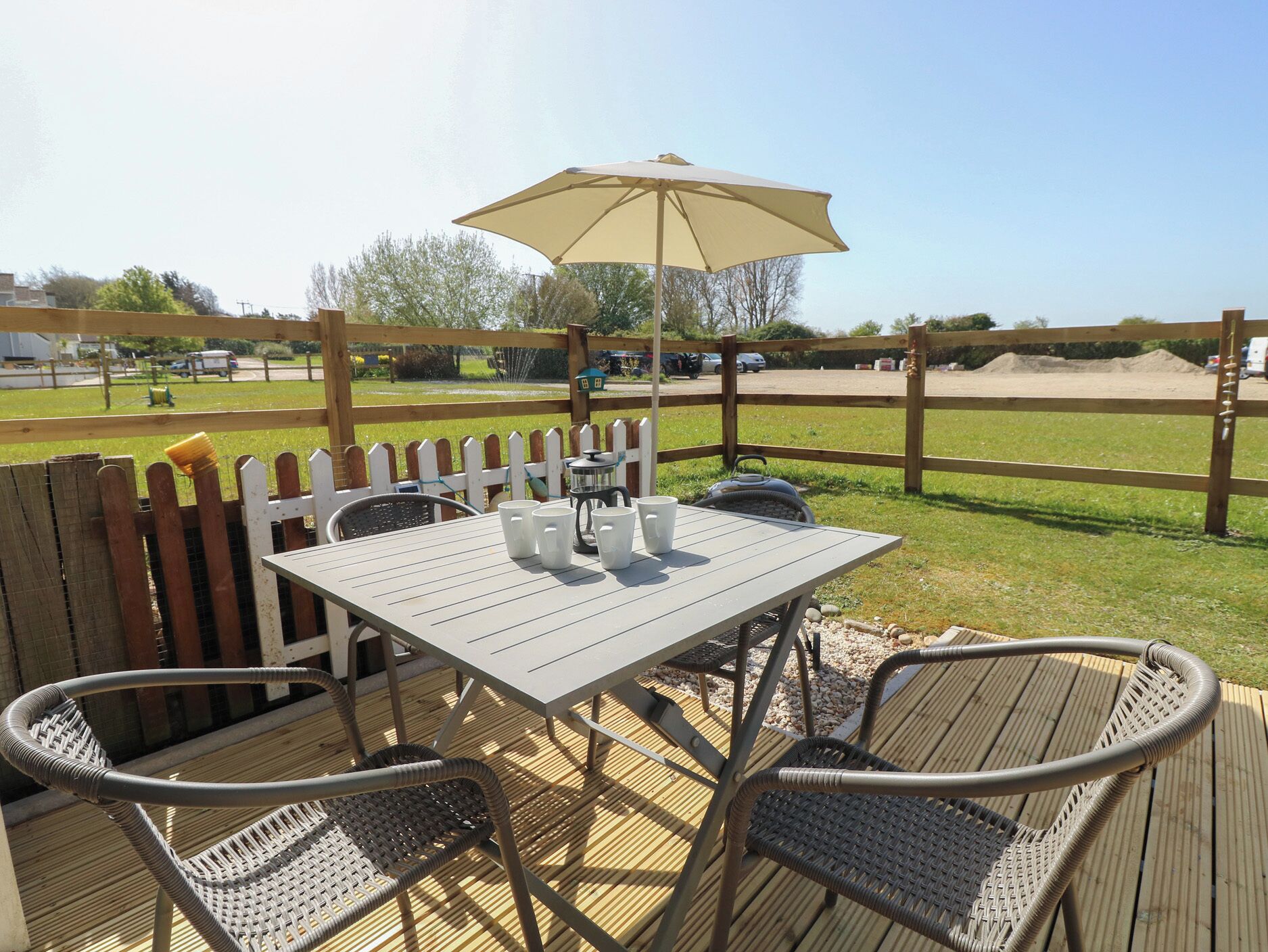 An outdoor patio with a table and chairs, a wooden fence, and a view of a grassy area.