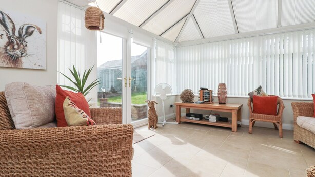 A spacious room with wicker furniture, a wooden coffee table, and a large window with blinds. - Bray Nook, 7 Craikewells (Bridlington)