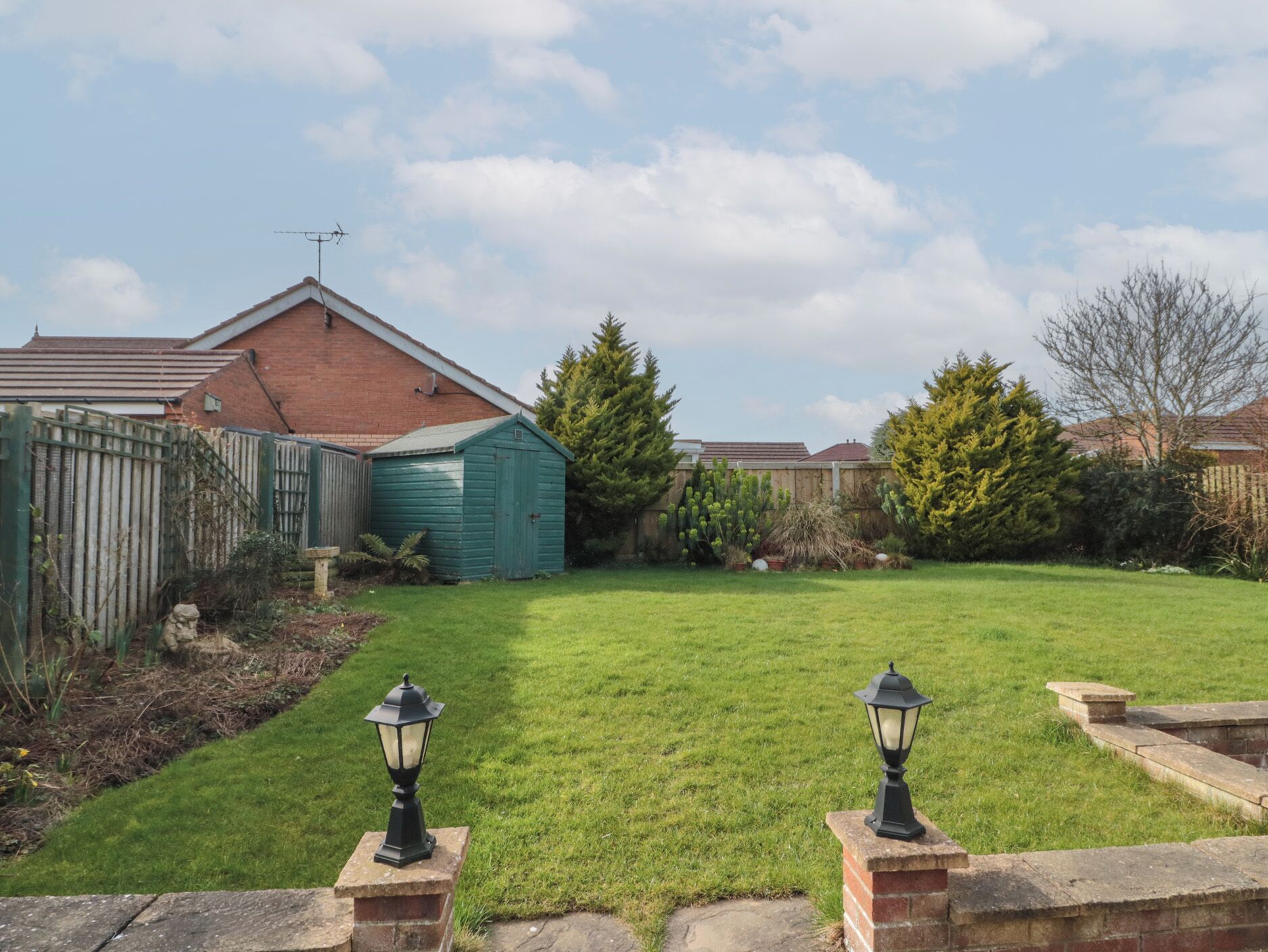 A well-maintained backyard with a green lawn, a wooden shed, and two black lantern-style lights.