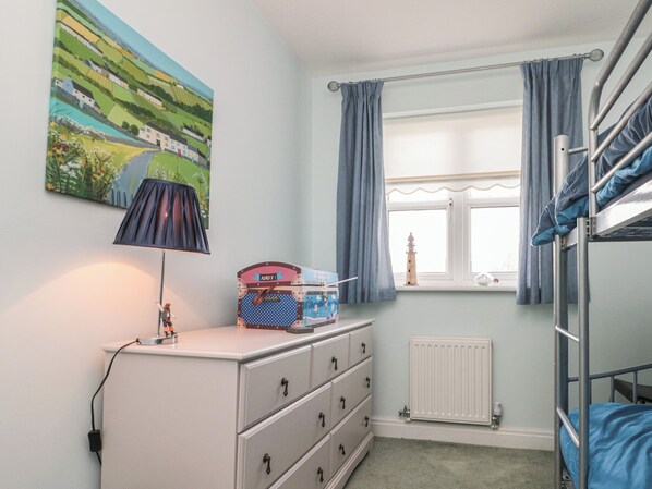 A child's bedroom with bunk beds, a dresser, a lamp, a painting, and a window with curtains.