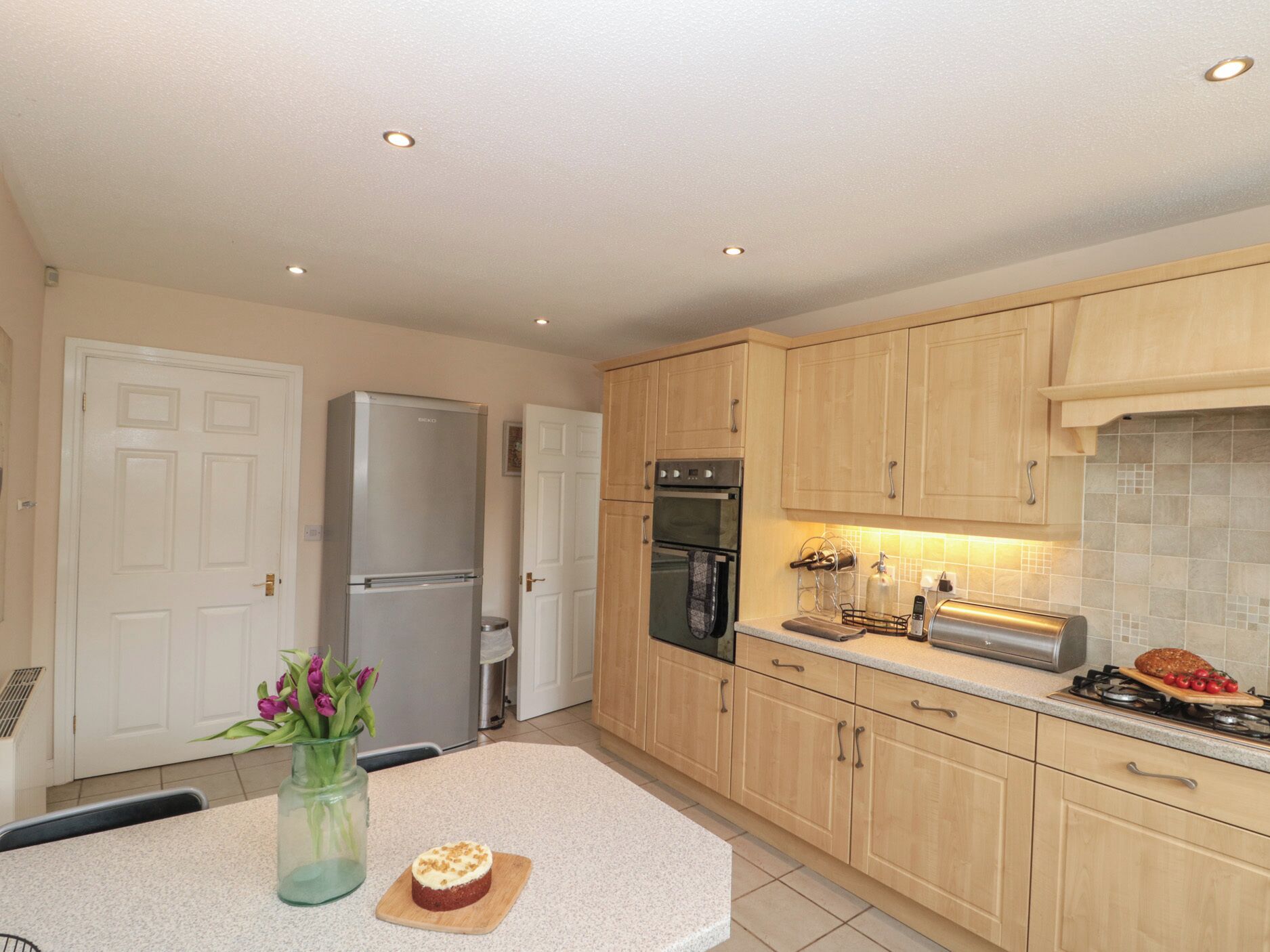 A modern kitchen with wooden cabinets, a stainless steel refrigerator, an oven, and a gas stove.