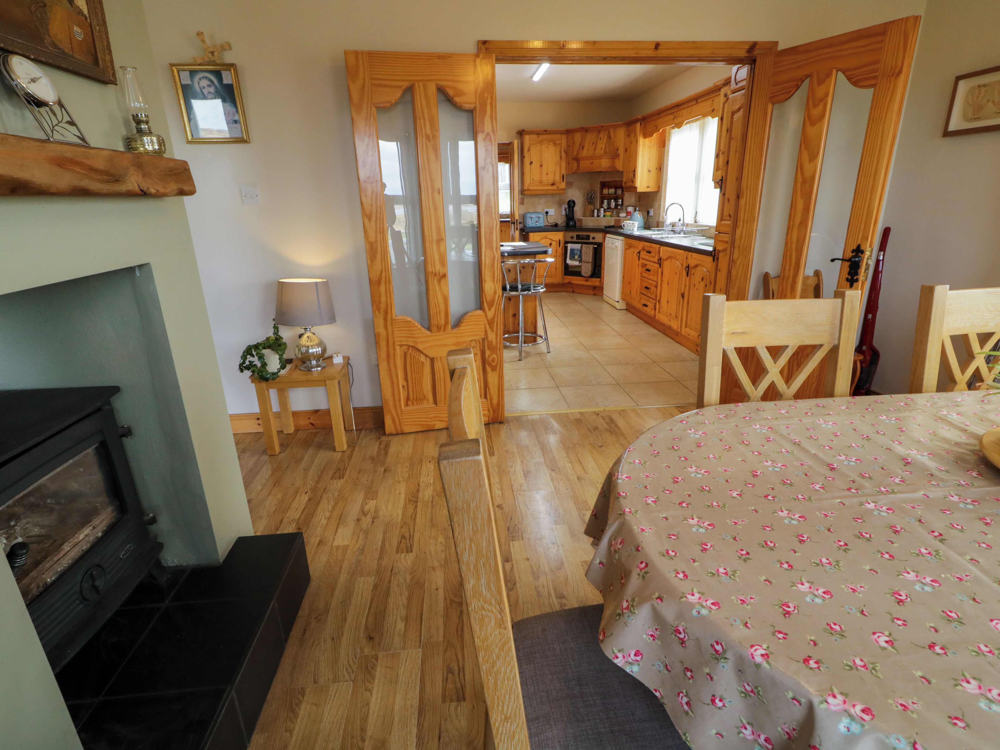 Una habitación acogedora con chimenea, una cama con colcha floral, suelo de madera, cocina con armarios de madera y un comedor con una silla.