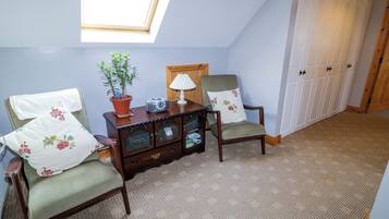 A room with two chairs, a small table with a lamp, a potted plant, and a wooden cabinet.