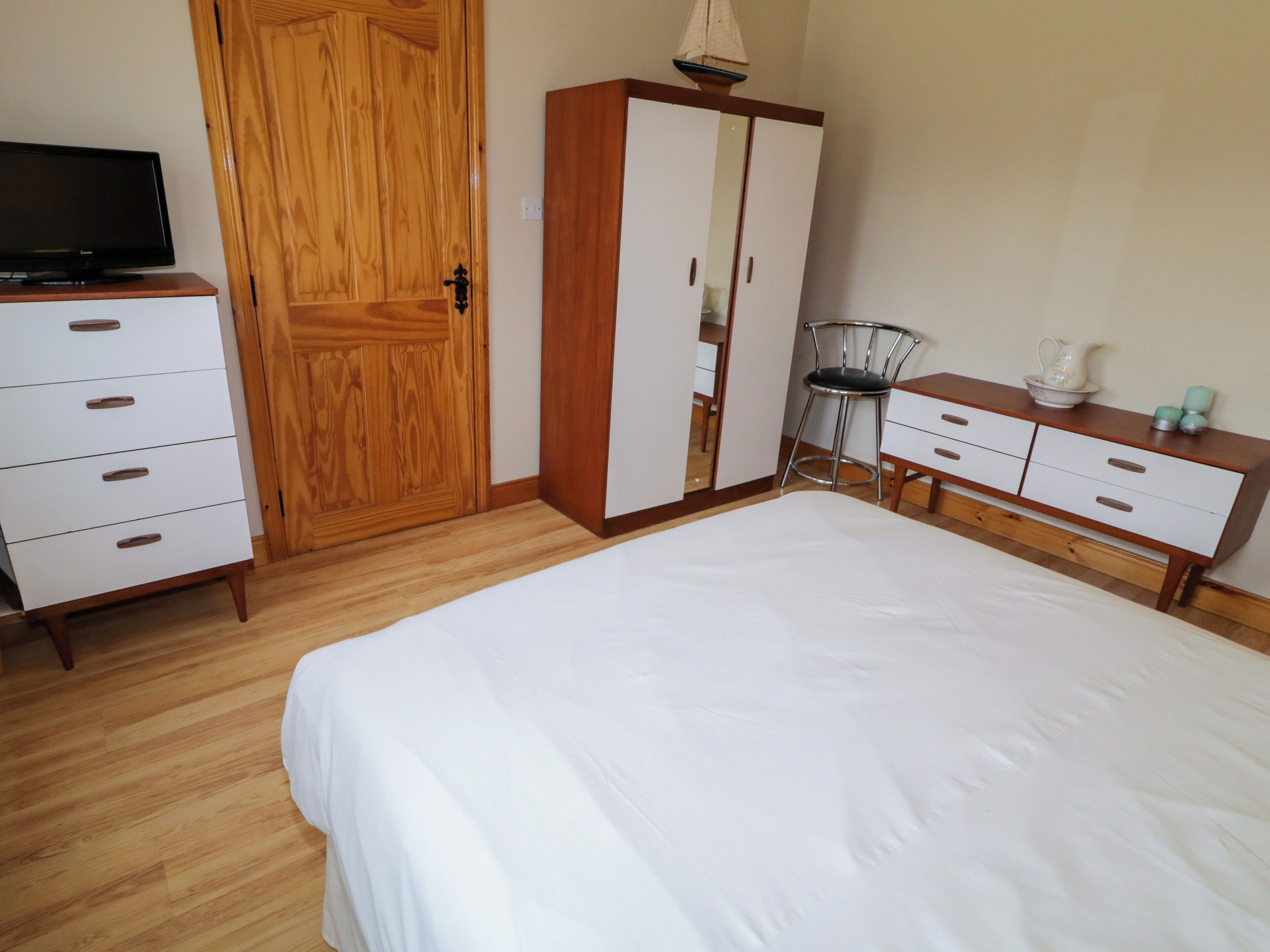 A bedroom with a bed, wooden wardrobe, a chair, and a television.