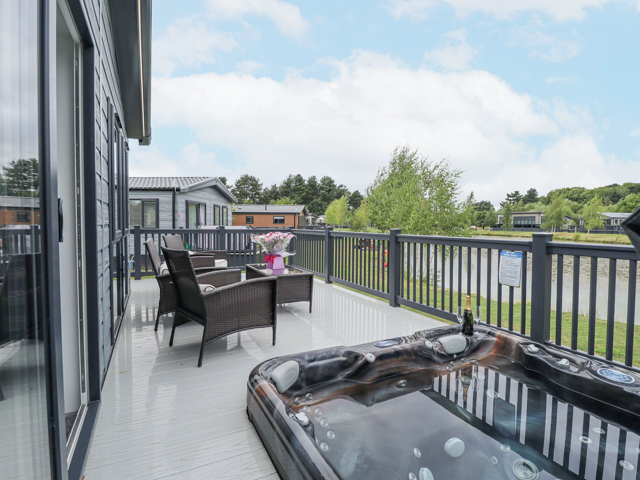 Un balcon agrémenté de meubles en osier, un jacuzzi et une vue sur un lac et des maisons.