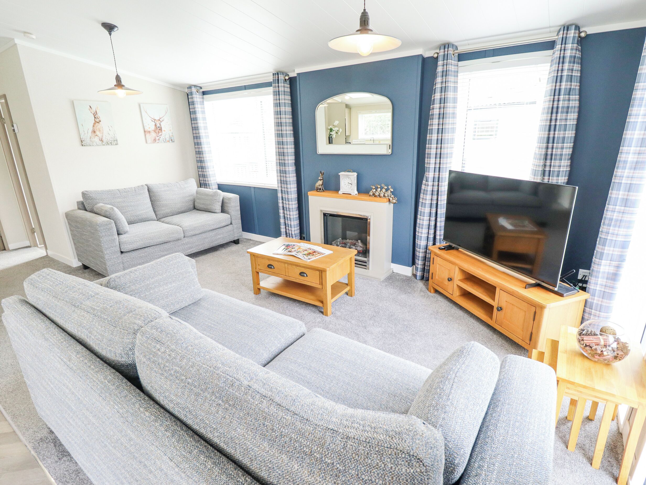 A living room with a grey sofa set, a wooden coffee table, a flat-screen TV on a wooden stand, and a fireplace.
