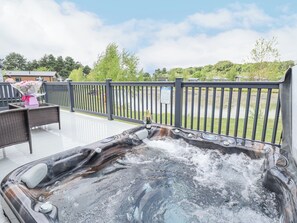 A hot tub on an outdoor deck with a view of a lake and trees. - Sunset Lodge (Woodhall Spa)