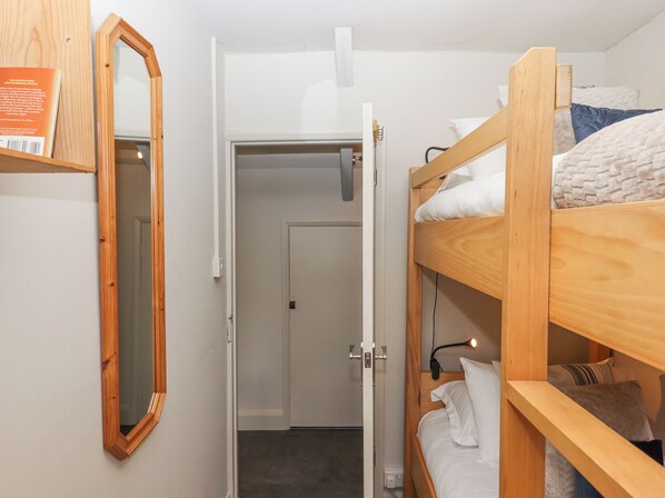 A bunk bed room with a wooden frame, a mirror, and a door leading to another room.