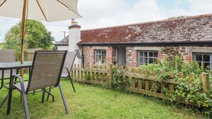 A stone house with a wooden fence, a table with chairs, and a large umbrella. - Hole Farm Stables (Newton Abbot)