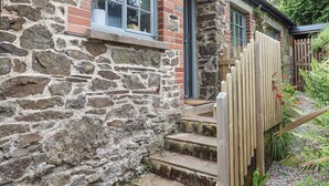 A stone building with a wooden staircase leading to a door, surrounded by greenery. - Hole Farm Stables (Newton Abbot)