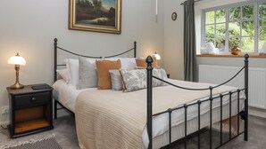 A neatly arranged bedroom with a bed, bedside lamps, a framed painting, and a window with curtains. - Hole Farm Stables (Newton Abbot)
