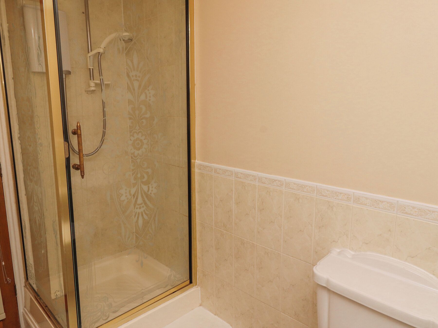 Ein Badezimmer mit Duschkabine, Toilette und beige gefliesten Wänden.