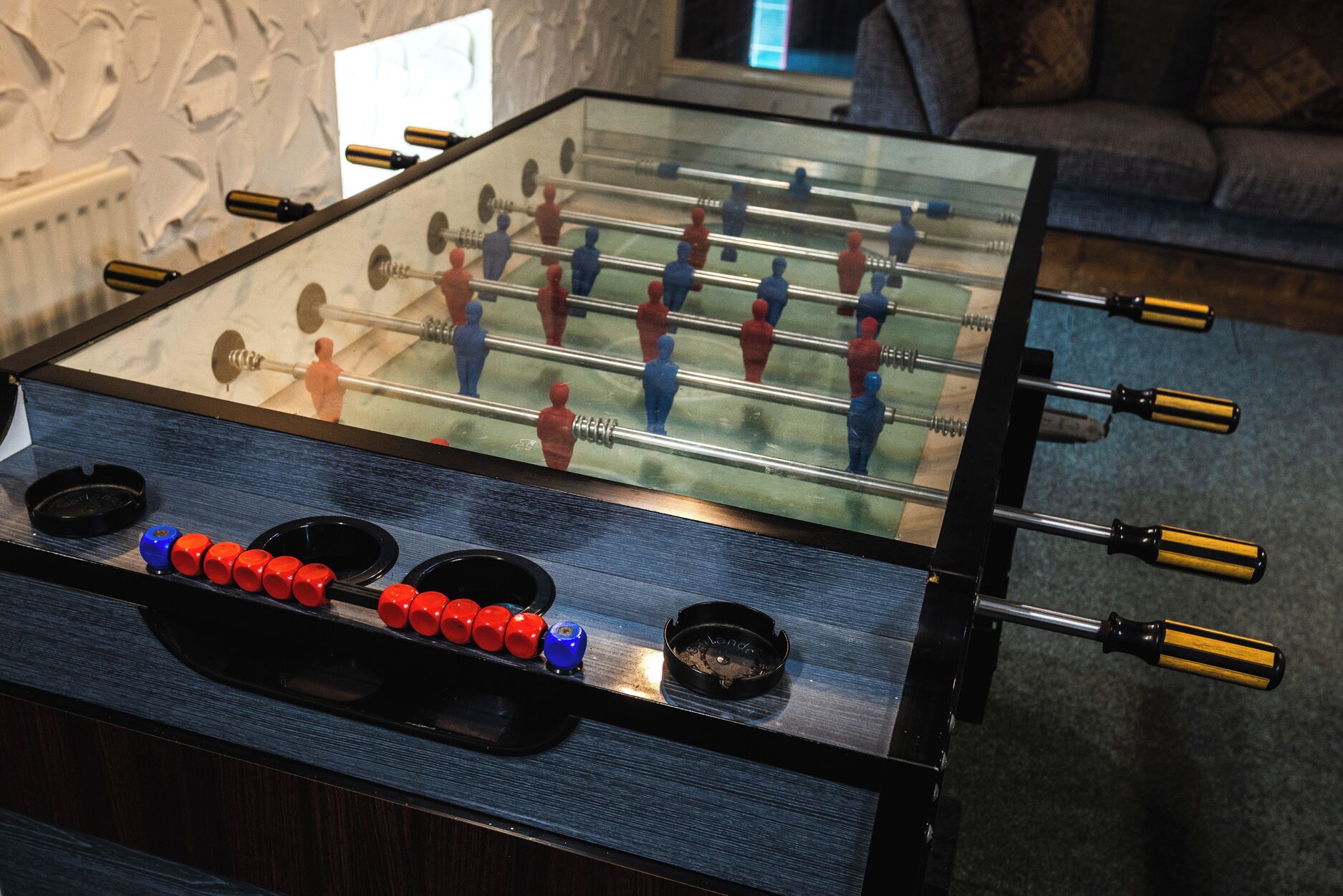 A foosball table with red, blue, and yellow figures, and a clear glass top.