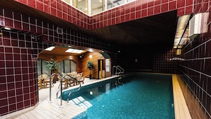 An indoor swimming pool with a tiled floor, a wooden lounge area with chairs, and a small wooden structure with a door. - Timberwick Green (Wooler)