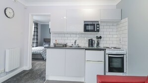 A compact kitchen with white cabinets, a microwave, a kettle, and a stove. - Flat 1A, Big Tree Holiday Flats (Paignton)
