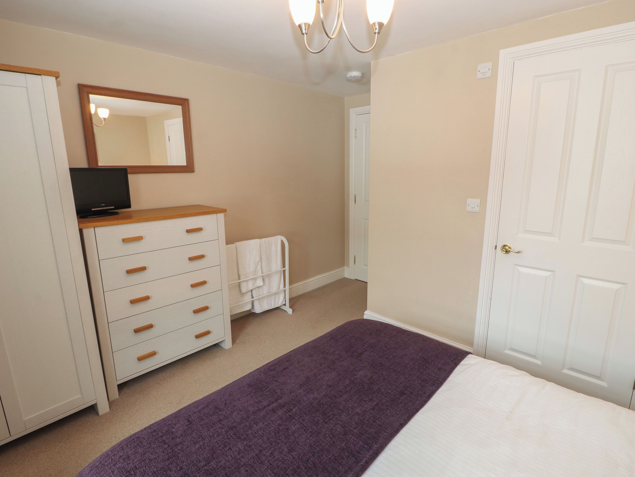 A bedroom with a bed, a dresser, a mirror, a television on the dresser, and a door.