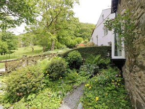 Un exuberante jardín con diversas plantas y flores, un muro de piedra y un edificio con fachada blanca.