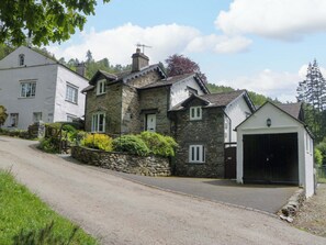 Ein Haus aus Stein mit Garage, Auffahrt und einer Steinmauer mit Bepflanzung.