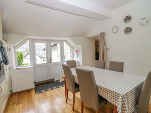 A dining area with a table and chairs, a window with a view, and a radiator. - Hollens Cottage (Ambleside)