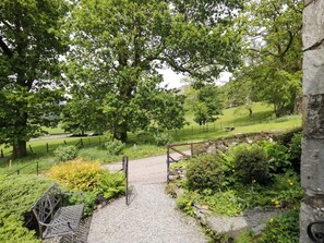 A pathway leading through a park with trees, a bench, and a stone wall. - Hollens Cottage (Ambleside)