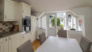 A kitchen with white cabinets, a stove, and a dining table with chairs. - Hollens Cottage (Ambleside)