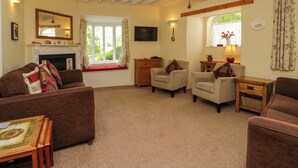 A cozy living room with a fireplace, comfortable seating, and a television. - Hollens Cottage (Ambleside)