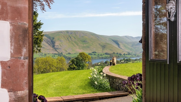 Une vue depuis l’entrée d’une maison, donnant sur un paysage verdoyant et luxuriant, avec un lac et des collines à l’horizon.